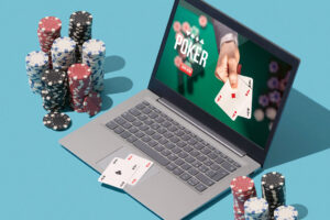 Kannettavan tietokoneen näytöllä pokeripeli ja tietokoneen vieressä pöydällä pelikortteja ja pelimerkkejä.