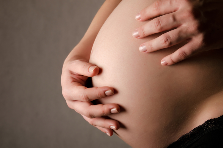 vaaleaihoisen naisen raskausvatsa, jossa kaksi kättä päällä