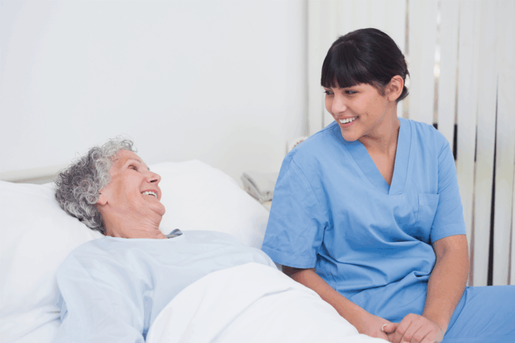 Iäkäs potilas sängyssä, vieressä hoitaja.